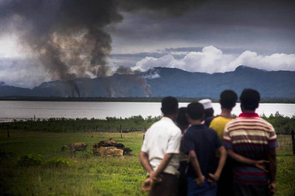 A group of Rohingya men helplessly watch their houses being burned down on the other side in their native village.