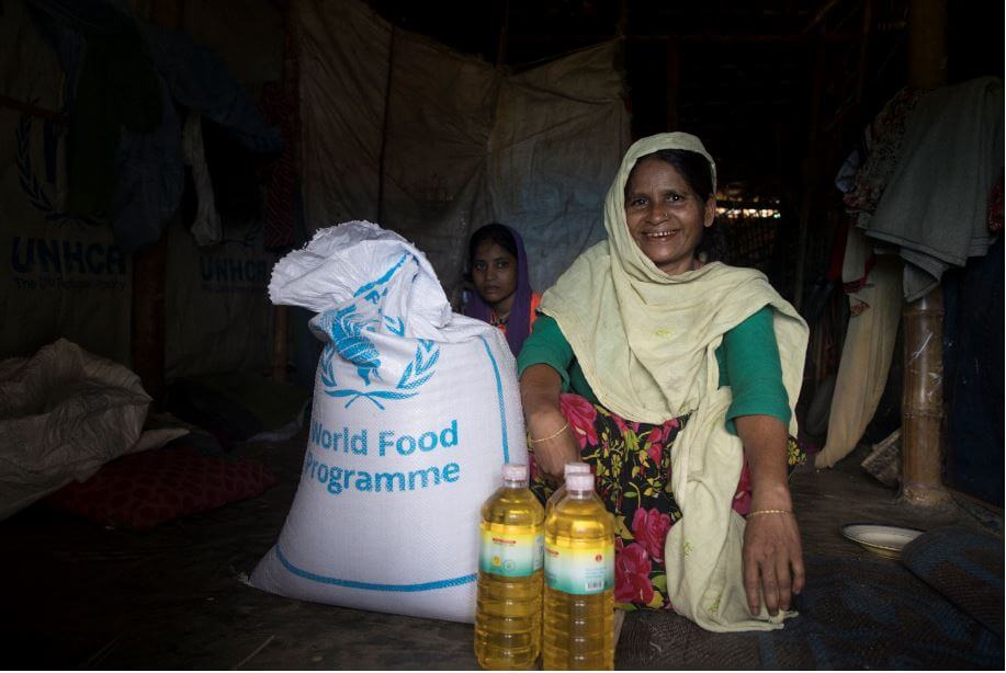 A Rohingya refugee woman with a bag of WFP food and bottles of vegetable oil in Cox's Bazar, Bangladesh